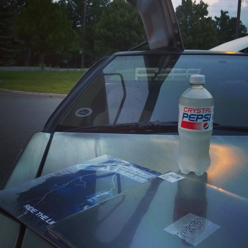 A bottle of Crystal Pepsi with Metallica's Ride the Lightning and
Joy Division's Unknown Pleasures vinyl records sitting on the hood of a
DeLorean